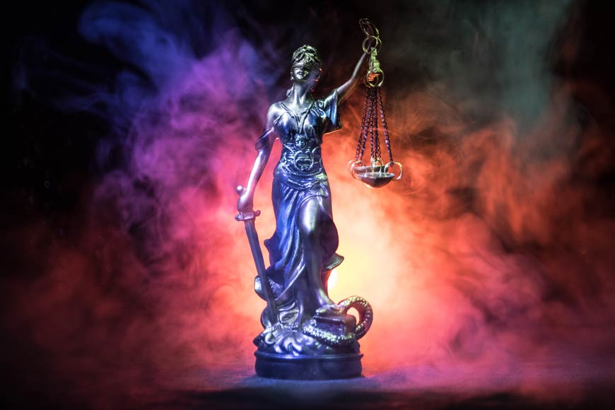 Photo of a statue of our lady justice with multi-colored fog and backlighting on dark background